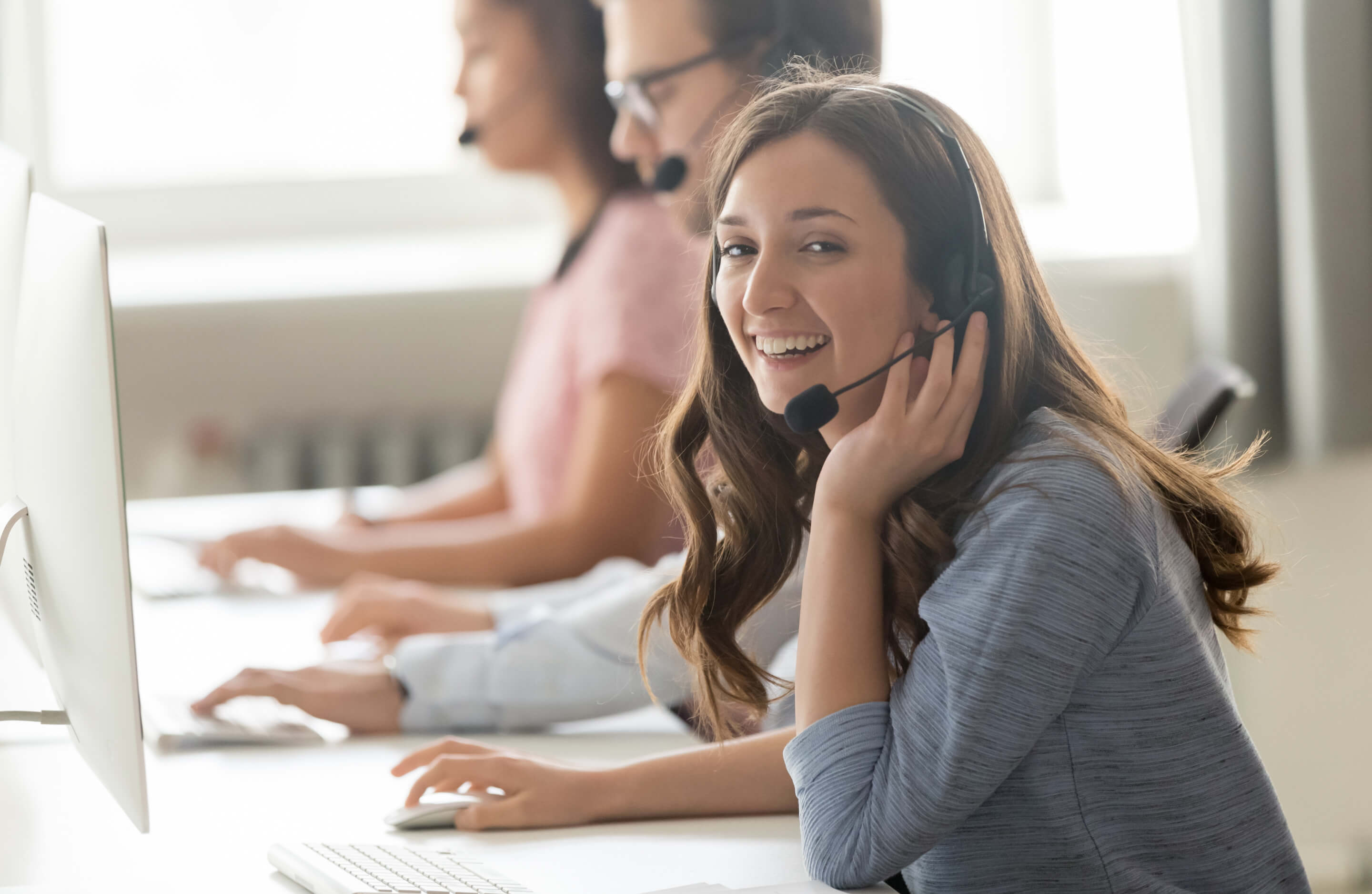 a woman with a headset smiling while working at a computer